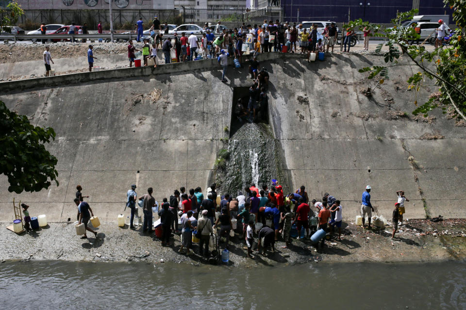 Venezuelans collect water flowing into a sewage canal from a broken pipe at the Guaire River in Caracas on March 11, 2019, as a massive power outage continues affecting some areas of the country amid a longstanding political crisis.&nbsp; (Photo: CRISTIAN HERNANDEZ via Getty Images)