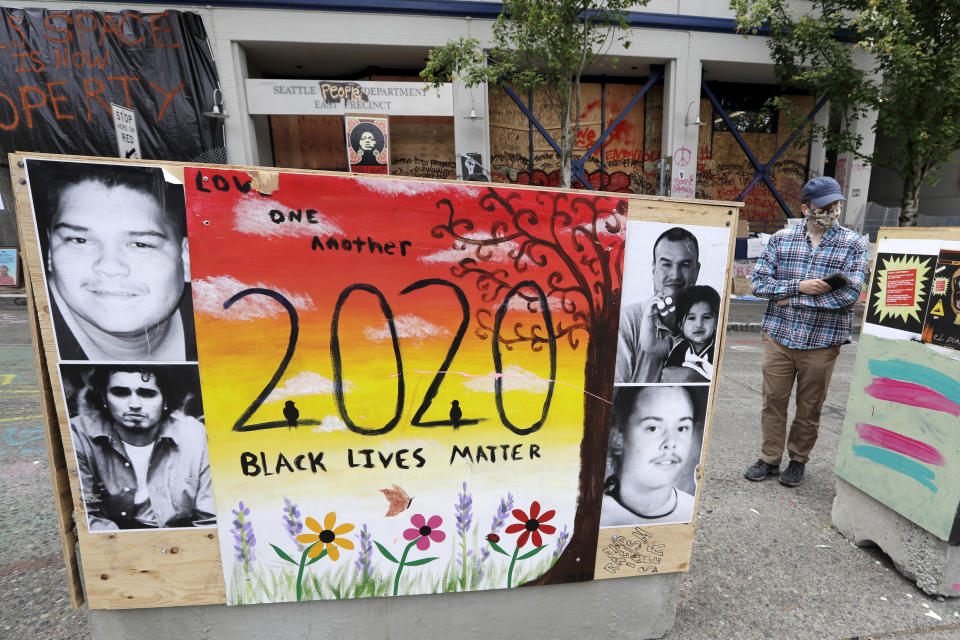 A man looks over artwork covering barricades in front of a boarded-up and closed Seattle police precinct Sunday, June 21, 2020, in Seattle, where streets are blocked off in what has been named the Capitol Hill Occupied Protest zone. Police pulled back from several blocks of the city's Capitol Hill neighborhood near the Police Department's East Precinct building earlier in the month after clashes with people protesting the death of George Floyd. (AP Photo/Elaine Thompson)