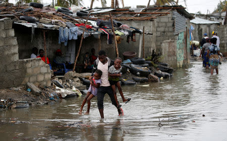 A man carries his children after Cyclone Idai at Praia Nova, in Beira, Mozambique, March 23, 2019. REUTERS/Siphiwe Sibeko