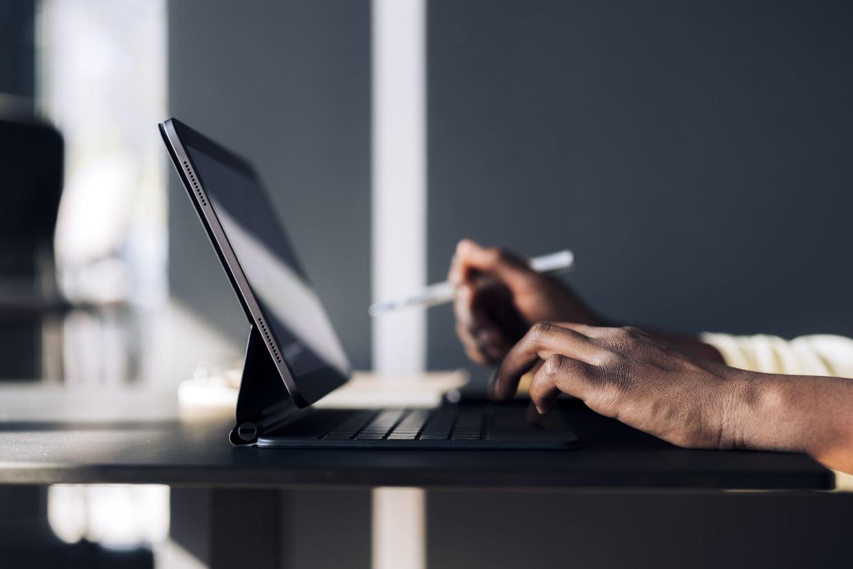 Unrecognizable African-American business woman typing notes on a keyboard while having online web conference on a digital tablet in a restaurant