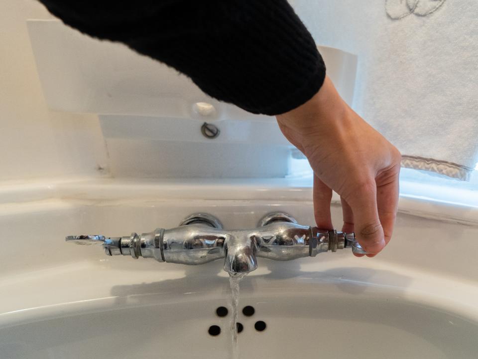 A hand turns on a faucet on a white sink