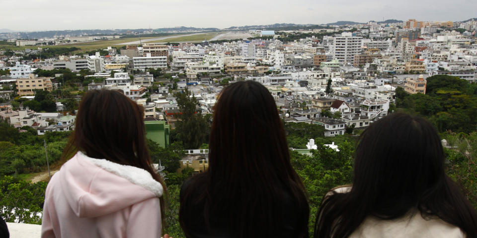 FILE - In this Dec. 17, 2009, file photo, high school students at an observation platform look at Marines Corps Air Station Futenma stretching beyond the residential area in Ginowan in Okinawa, southern Japan. President Donald Trump is raising a large chunk of the money for his border wall with Mexico by deferring several large military construction projects slated for the strategically important Pacific outpost of Guam. This may disrupt plans to move Marines to Guam from Japan and to modernize important munitions storage for the Air Force. About 7% of the funds for the $3.6 billion wall are being diverted from eight projects in U.S. territory. (AP Photo/Shizuo Kambayashi, File)
