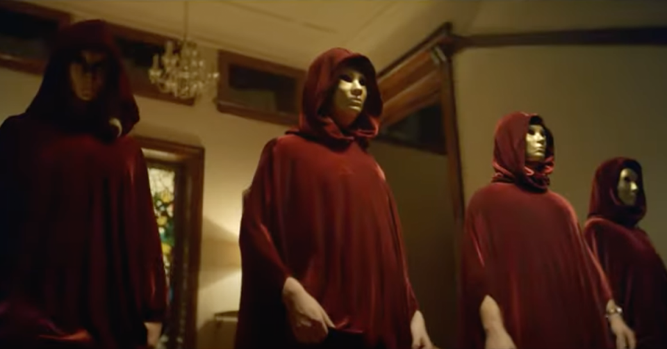 The Traitors dressed in red hooded cloaks with gold masks.