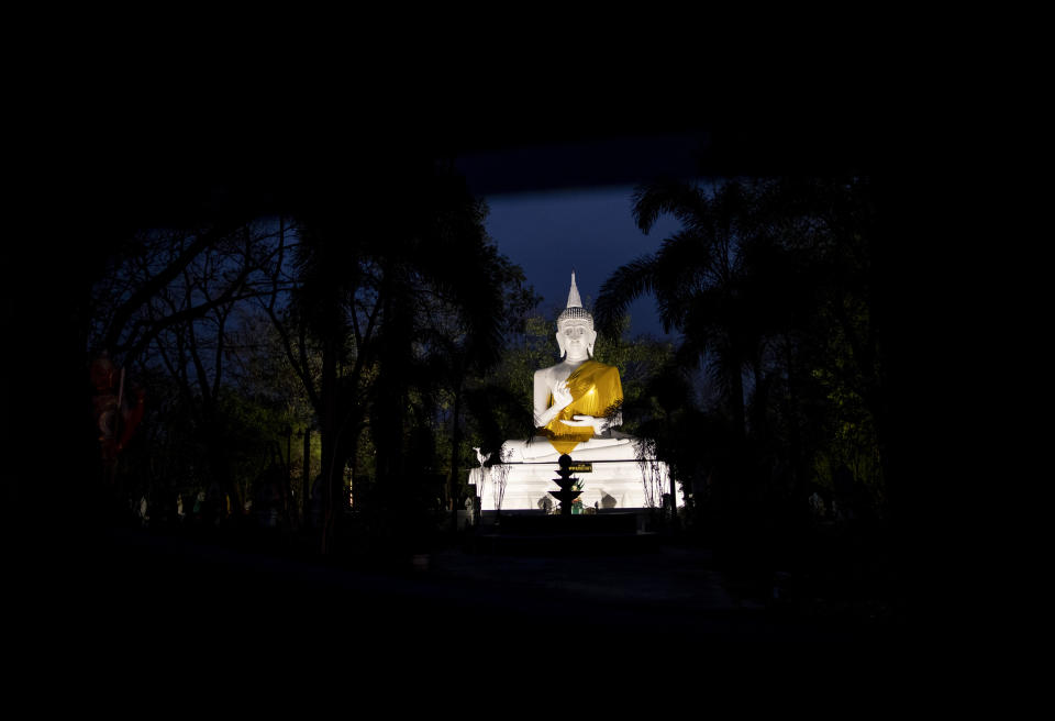 In this Monday, Feb. 10, 2020, photo, an illuminated Buddha statue at Wat Pa Sattharuam Buddhist temple seen through trees in Nakhon Ratchasima, Thailand. The secluded temple complex in the northeastern Thai province had opened its gates for Buddha Day, allowing in dozens of devotees, when a rogue soldier from the neighboring Army base roared through in a stolen Humvee, fatally shooting nine people, including a 13-year-old boy, and injuring more. (AP Photo/Gemunu Amarasinghe)