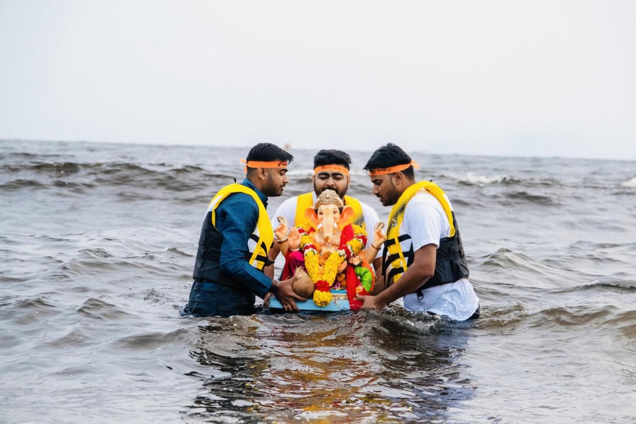 Akshay Dholariya, Rushi Mehta and Jeetendra Singh submerge a Hindu idol in waters of Mispec Beach in a ceremonial act as part of a festival. (Submitted by Sravan Yemineni - image credit)