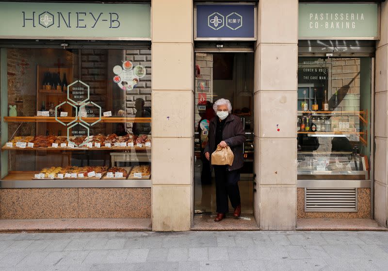 Elderly woman wears a protective face mask as she carries a bag with food products in Barcelona