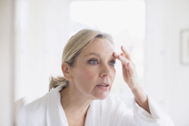 Mature woman touching eyebrow at bathroom mirror