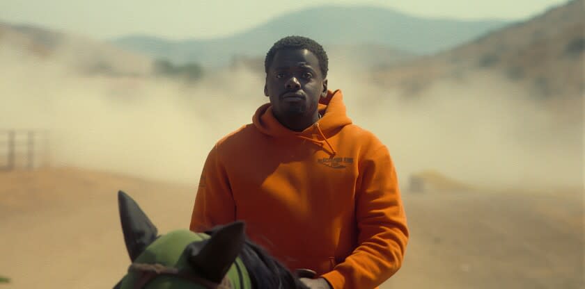 A man in an orange hoodie riding a horse in the desert