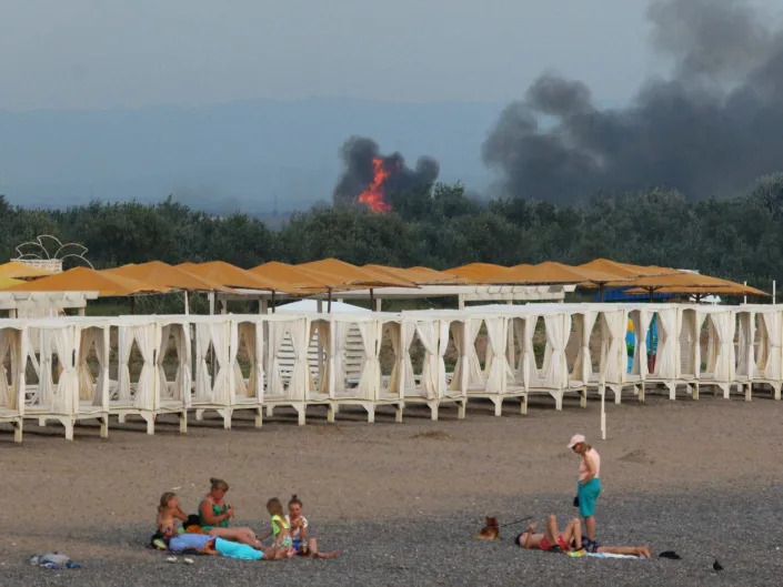 People on a beach as smoke and flames rise after explosions at a Russian military airbase, in Novofedorivka, Crimea August 9, 2022.