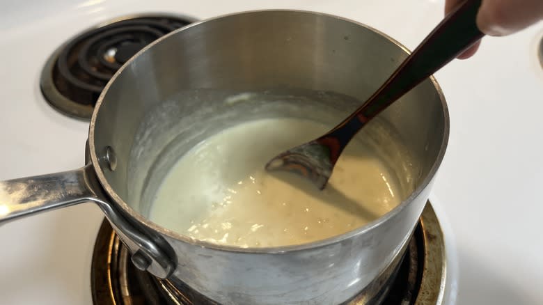 hand stirring rice pudding in a pot with a wooden spoon