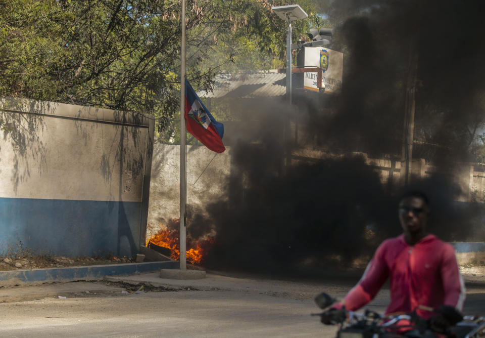 A taxi driver passes a burning tire outside the door of police headquarters placed by officers protesting bad police governance in Port-au-Prince, Haiti, Thursday, Jan. 26, 2023. Haiti's nearly 200 gangs have taken advantage of the chaos, warring for control. (AP Photo/Odelyn Joseph,File)