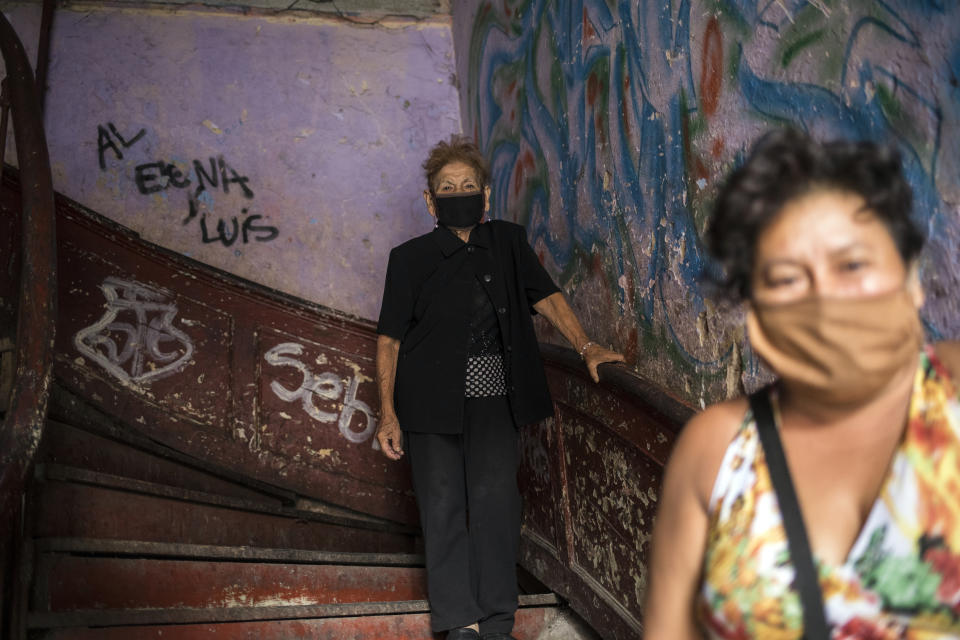 In this March 29, 2020 photo, 72-year-old Maria Isabel Aguinaga, wearing a protective face mask, descends the stairs of her crumbling residential building nicknamed “Luriganchito” after the country’s most populous prison, in Lima, Peru. To try to address the coming humanitarian disaster, Peru has begun distributing about $400 million to feed 12 million poor people for one month. But the money doesn't seem to be reaching most of the families in the sprawling shared house. (AP Photo/Rodrigo Abd)