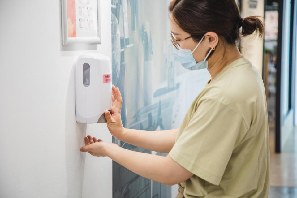 Asian woman wearing face mask cleaning her hand with hand sanitizer in an office setting