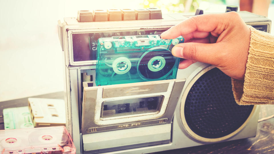 Retro lifestyle - Woman hand holding tape cassette with cassette player and recorder for listen music - vintage color tone effect.