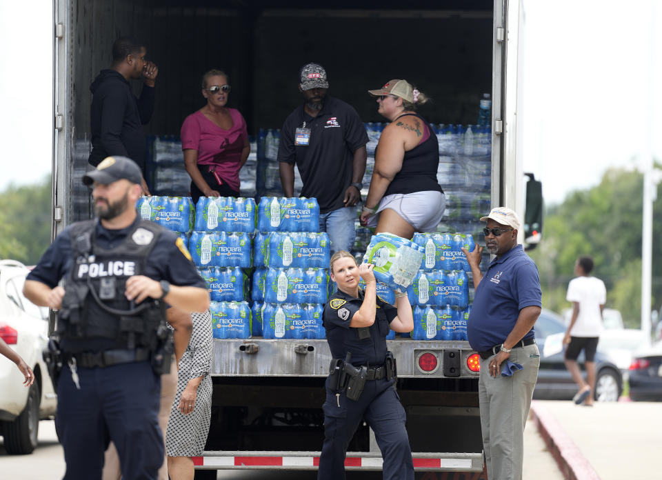 A Houston police officer carries a case of water to a car outside of Sunnyside Health and Multi-Service Center during a distribution of water and ice on Wednesday, July 10, 2024, after Hurricane Beryl hit the Houston area on Monday. (Karen Warren/Houston Chronicle via AP)