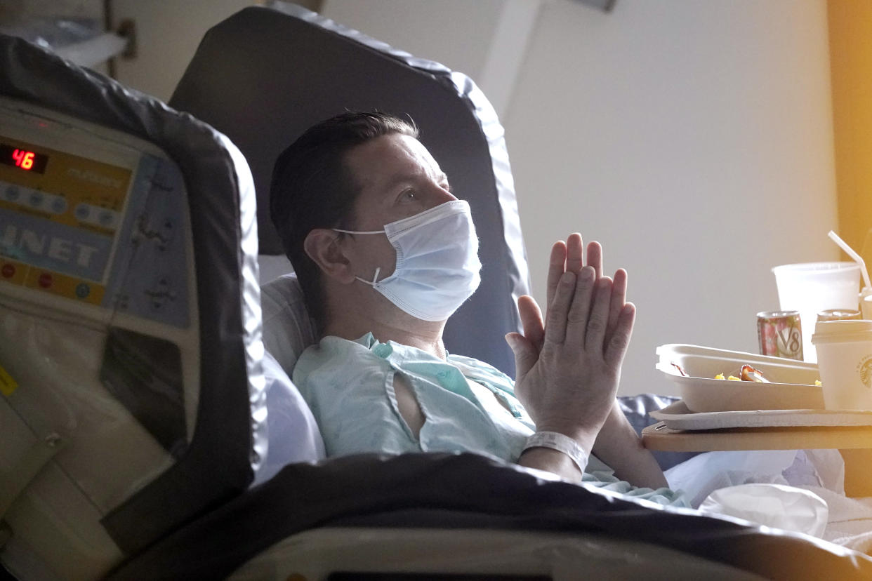 A man lies in a hospital bed while wearing a mask.