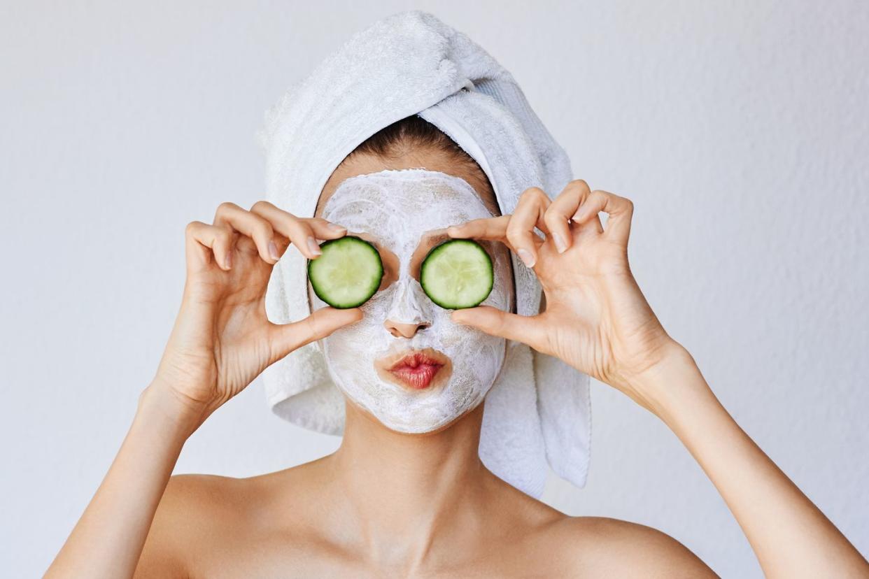 beautiful young woman with facial mask on her face holding slices of fresh cucumber