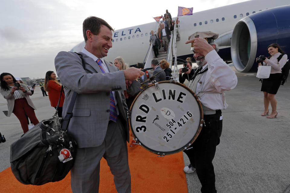 Clemson coach Dabo Swinney plays the cymbal on the drum of a member of the 3rd Line Brass Band as he arrives with the team for the NCAA College Football Playoff title game in New Orleans, Friday, Jan. 10, 2020. Clemson is scheduled to play LSU on Monday. (AP Photo/Gerald Herbert)