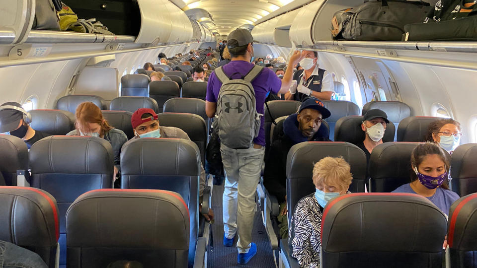 Passengers, mainly wearing masks, wait in their seats as others wait in the aisle to find their places.