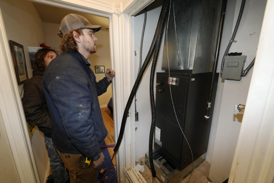 John Paul, front, and David Valenzuela work to install a heat pump in an 80-year-old rowhouse Friday, Jan. 20, 2023, in northwest Denver. (AP Photo/David Zalubowski)