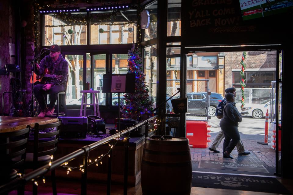 Jacob Reynolds performs at the Cerveza Jack while two pedestrians walk past the restaurant on 2nd Avenue in Nashville, Tenn., Tuesday, Dec. 19, 2023.