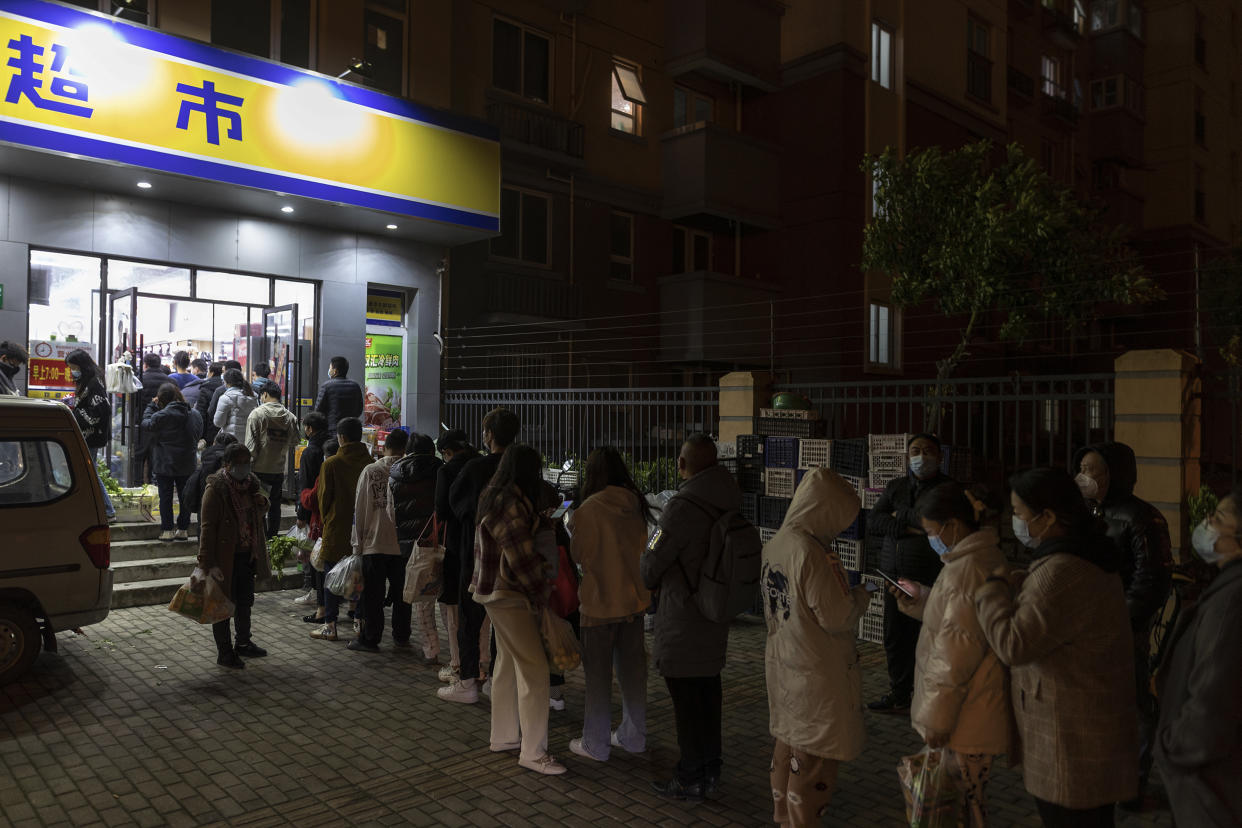 Residents wearing face masks to help protect from the coronavirus line up outside a supermarket at night to buy groceries in Shanghai. (AP)