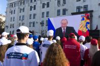 FILE - People watch Russian President Vladimir Putin's address as they gather during celebrations marking the incorporation of the Luhansk region into Russia in Luhansk, Ukraine, Friday, Sept. 30, 2022. The signing of the treaties making the four regions part of Russia follows the completion of the Kremlin-orchestrated "referendums." Words on their ti-shorts are reading "Volunteers for Russia, With Russia forever!". (AP Photo, File)