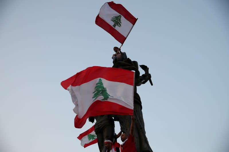 Demonstrators wave Lebanese national flags as they stand atop a statue on Martyrs' square during an anti-government protest in downtown Beirut
