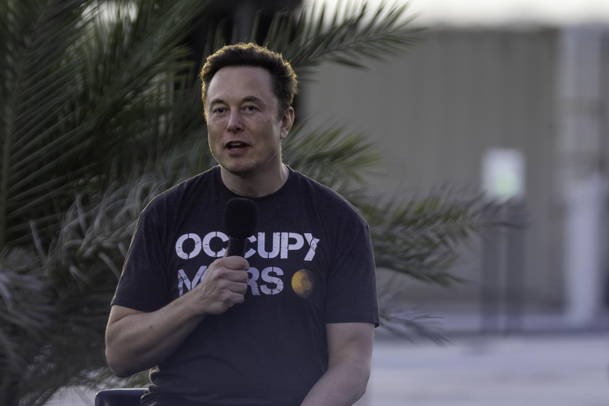 Elon Musk holds a microphone.