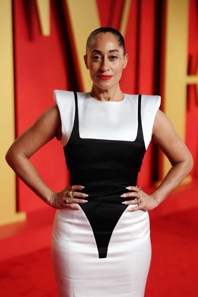 Person on red carpet in a sleeveless black and white fitted dress with hands on hips