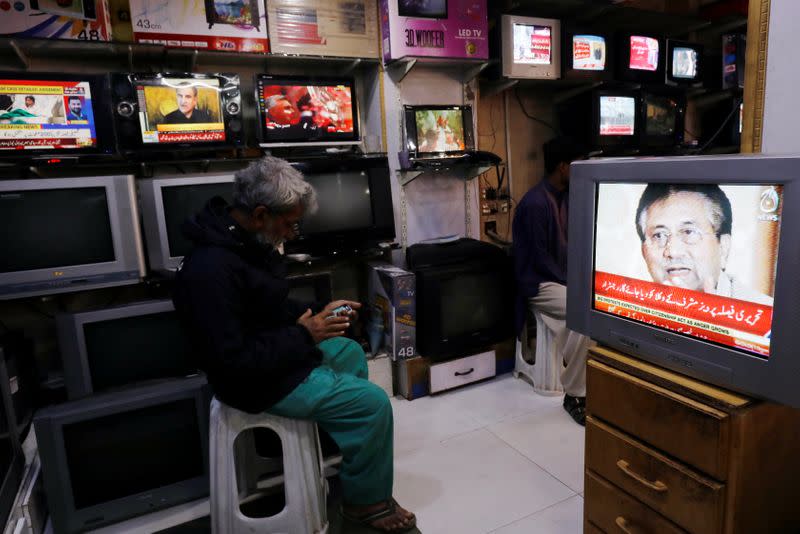 A man dials his cellphone near a television displaying the news of detailed verdict after Pakistani court sentenced former military ruler Pervez Musharraf to death on charges of high treason and subverting the constitution, at a shop in Karachi,