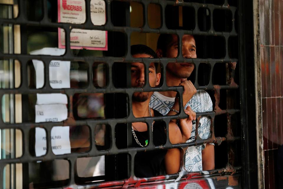 Men take cover and watch from inside a bakery after the Bolivarian National Guard arrived during clashes between motorcyclists and residents of the Los Ruices neighborhood of Caracas, Venezuela, Thursday, March 6, 2014. Venezuelan officials say a National Guard member and a civilian were killed during the clash between residents and armed men who tried to remove a barricade placed by anti-government protesters. (AP Photo/Fernando Llano)