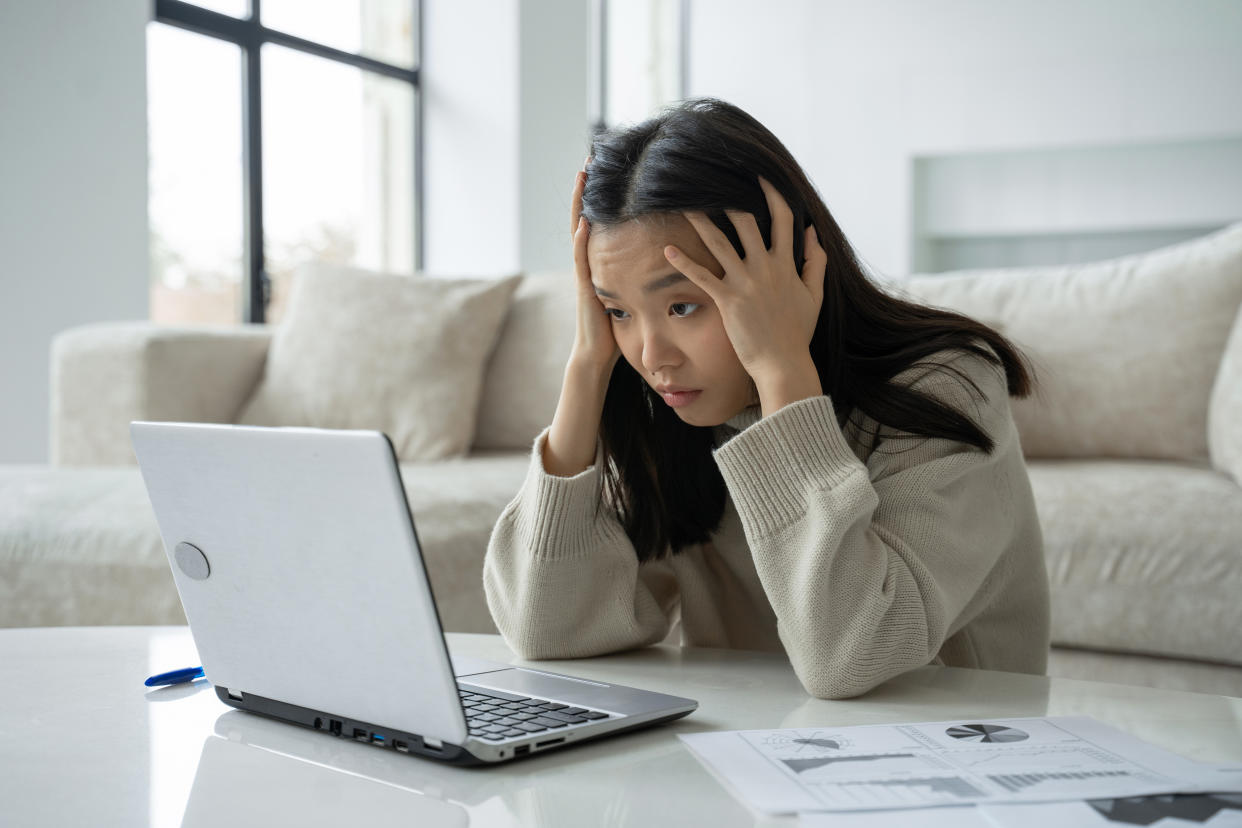 Tired, exhausted Asian woman with a laptop, problems with the project, feeling depressed, laziness in the home office in the living room.