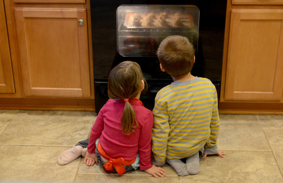 Two children sit on the floor watching cookies bake in an oven