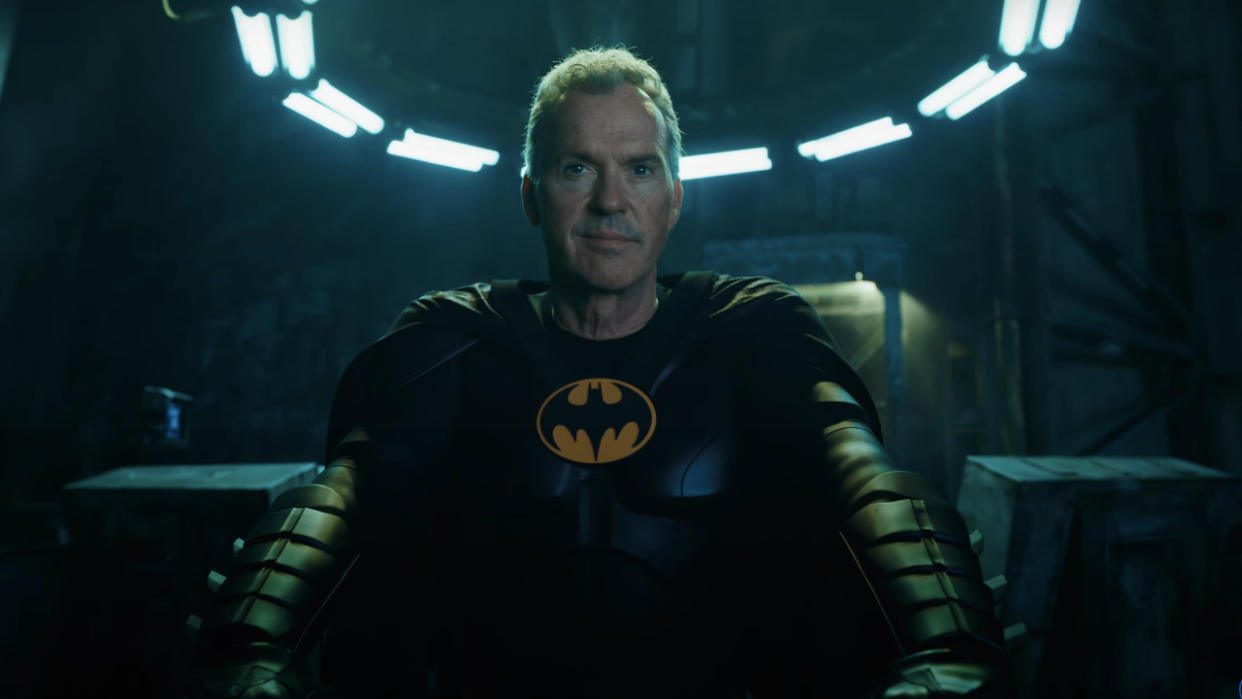  Michael Keaton smirking in his batsuit, with his cowl off, in the Batcave in The Flash. 