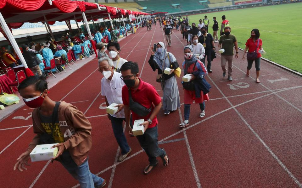 People leave the stadium with a snack box given to them after receiving a jab during a vaccination campaign in Bekasi - AP