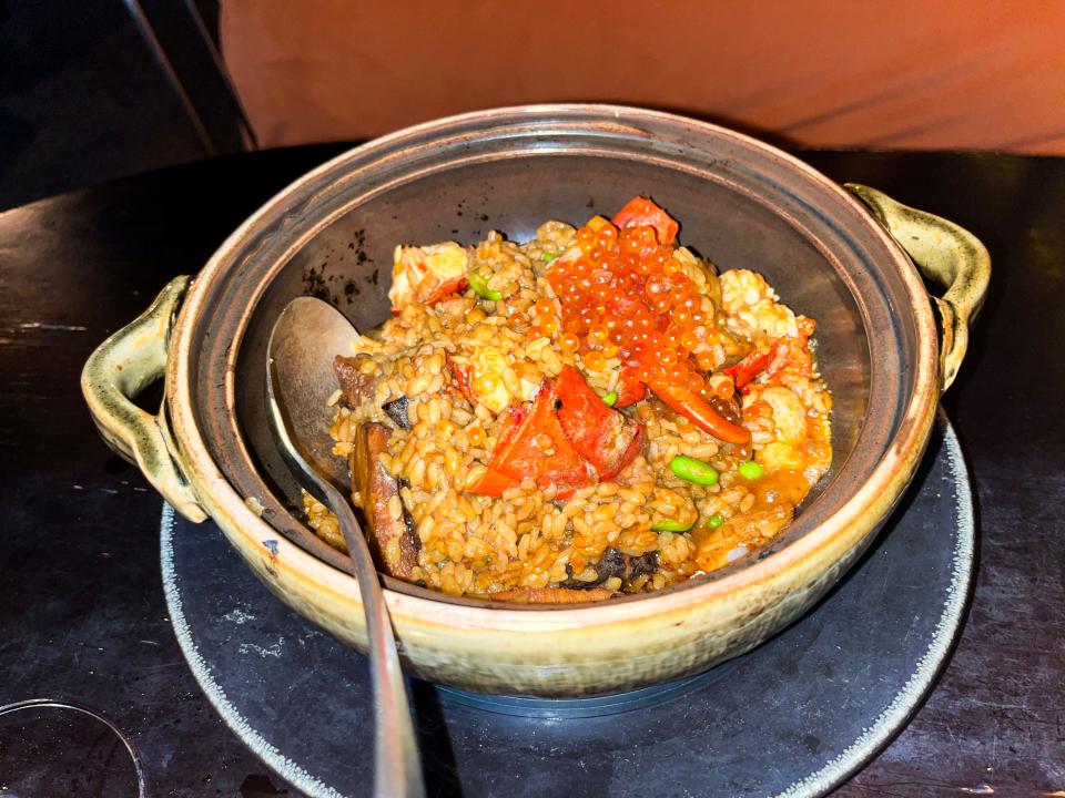 A bowl with two handles filled with rice with pieces of lobster, caviar, and edamame in it