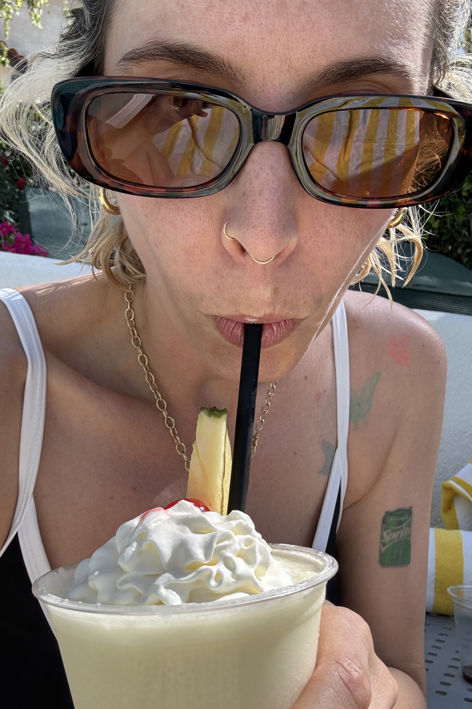 Woman sipping a tropical drink, garnished with fruit, at an outdoor café