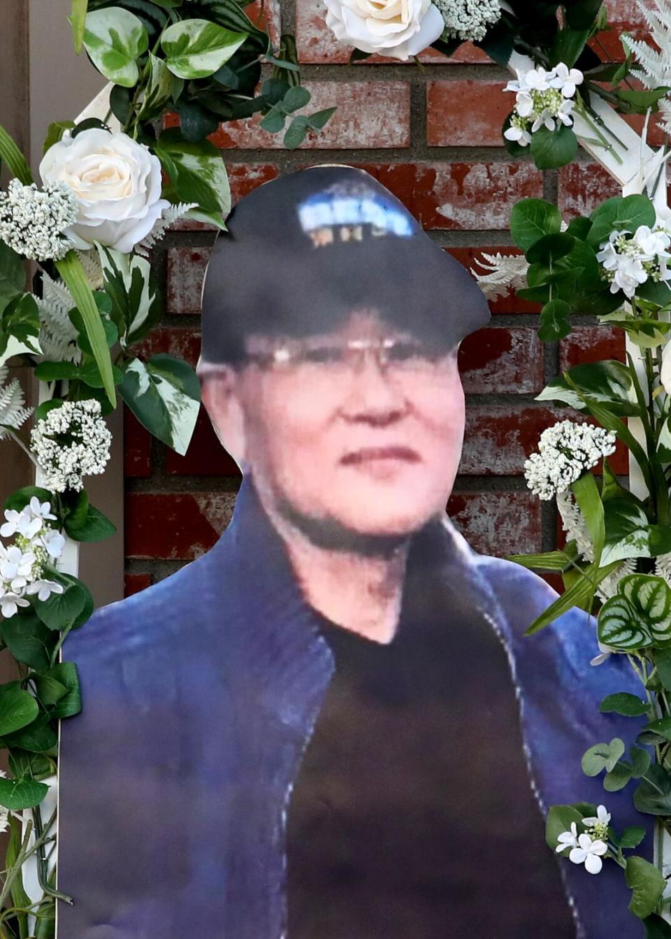 A cutout paper portrait of a man in a cap, blue sweater and wearing glasses, surrounded by a wreath of flowers