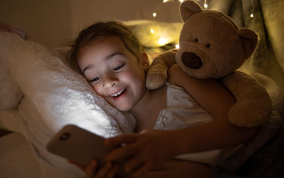 fille est au lit avec un ours en peluche et utilise un smartphone.  - iStockphoto