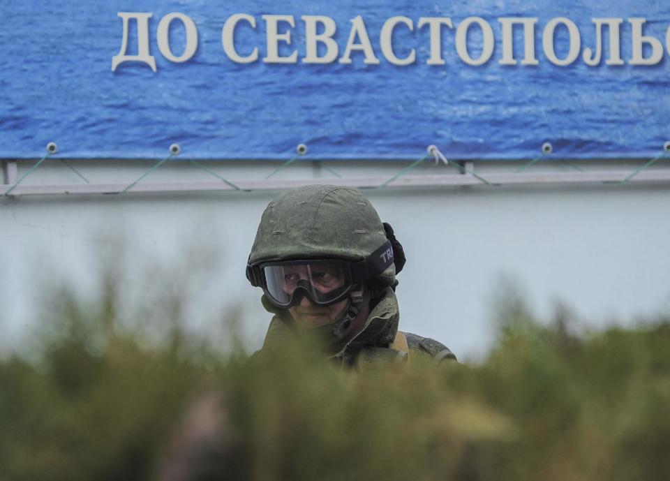 A gunman in unmarked uniform stands guard as troops take control the the Coast Guard offices in Balaklava, outskirts of Sevastopol, Ukraine, Saturday, March 1, 2014. The word in the background reads "To Sevastopol". An emblem on one of the vehicles and their number plates identify them as belonging to the Russian military. Ukrainian officials have accused Russia of sending new troops into Crimea, a strategic Russia-speaking region that hosts a major Russian navy base. (AP Photo/Andrew Lubimov)