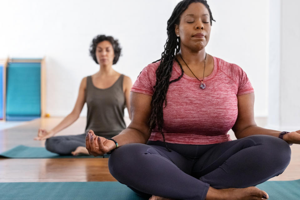 Two individuals practicing meditation in a yoga pose on mats indoors