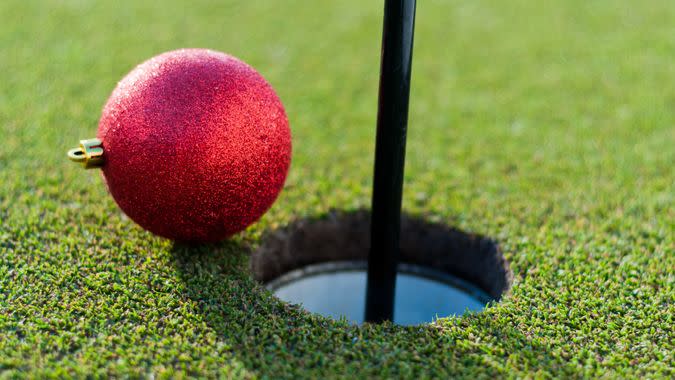 A bright red Christmas bauble rolling into a golf hole.