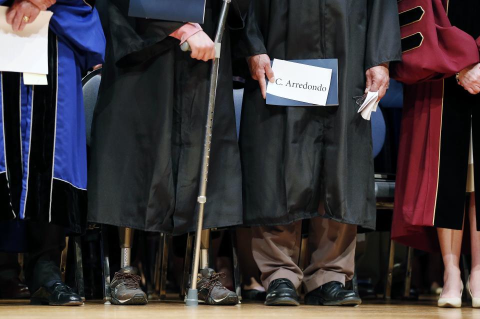 Boston Marathon bombing survivor Jeff Bauman, center left, stands on the dais with first-responder Carlos Arredondo, center right, during commencement ceremonies for Fisher College in Boston, Saturday, May 10, 2014. (AP Photo/Michael Dwyer)