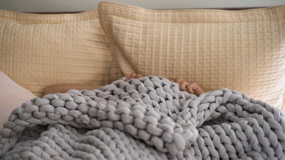 A weight blanket, which is a fibromyalgia self-care strategy, on a bed with yellow pillows