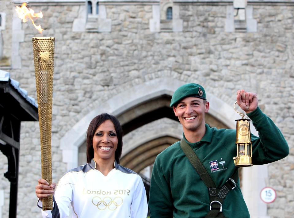 LONDON, ENGLAND - JULY 20: Dame Kelly Holmes and Marine Martyn Williams (R) pose with the Olympic Torch and Olympic Flame as the flame arrives in London during the London 2012 Olympic Torch Relay on July 20, 2012 in London, England. The Olympic Flame is now on day 63 of a 70-day relay involving 8,000 torchbearers covering 8,000 miles. (Photo by Jan Kruger/Getty Images)
