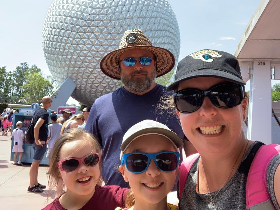 the writer, her partner, and two kids smiling in front of the epcot ball