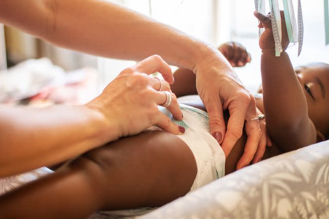 <p>Getty</p> Mom changing baby's diaper as they play with a toy (stock image)