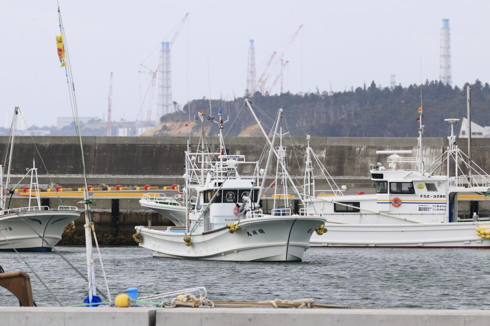 Fishing boats are seen at Ukedo port with a backdrop of Fukushima Daiichi nuclear power plant in Namie town, Fukushima prefecture, northeastern Japan, Tuesday, April 13, 2021, Japan's government decided Tuesday to start releasing massive amounts of treated radioactive water from the wrecked Fukushima nuclear plant into the Pacific Ocean in two years - an option fiercely opposed by local fishermen and residents. (Yusuke Ogata/Kyodo News via AP)