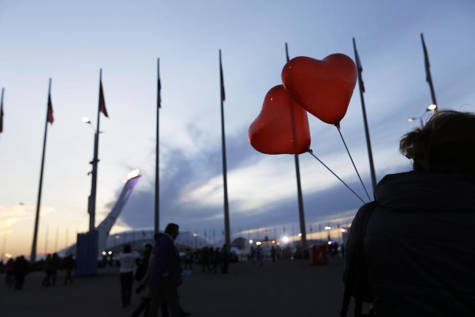 The Olympic flame burns in the background as a visitor walks through the Olympic Park with heart shaped balloons in celebration of Valentine's Day at the 2014 Winter Olympics, Friday, Feb. 14, 2014, in Sochi, Russia. (AP Photo/David Goldman)